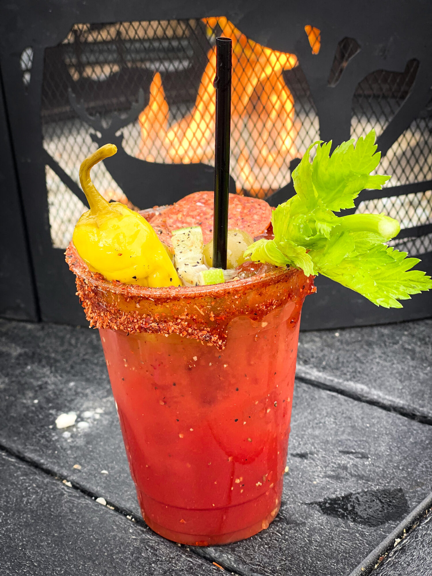 Bloody Mary drink with celery, pepperoni and pepperoncinis by the fire.