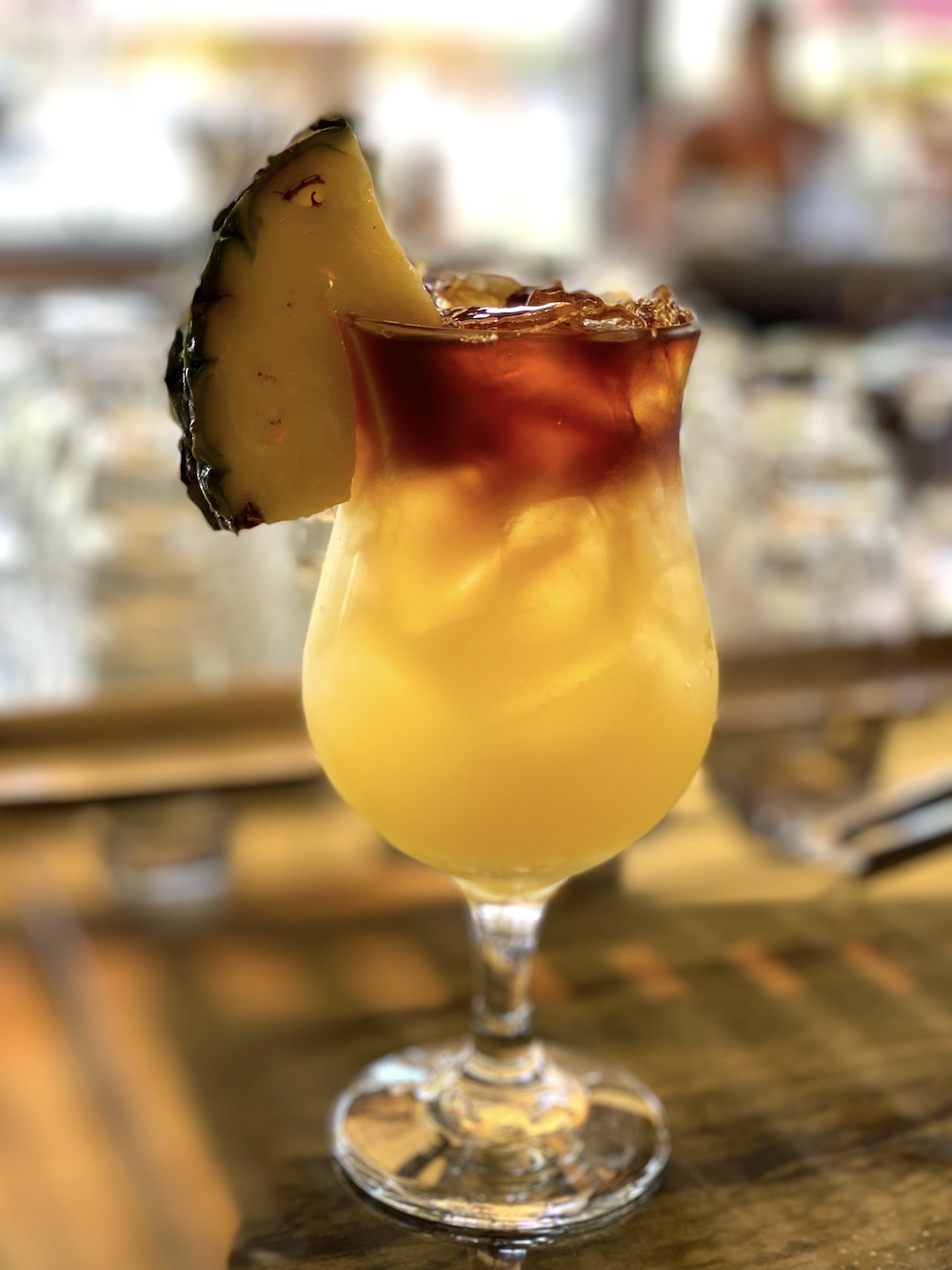 Celebrate summer by making Mai Tai for a Crowd! Photo of Mai Tai with pineapple juice, rum float and pineapple wedge in a tall glass.
