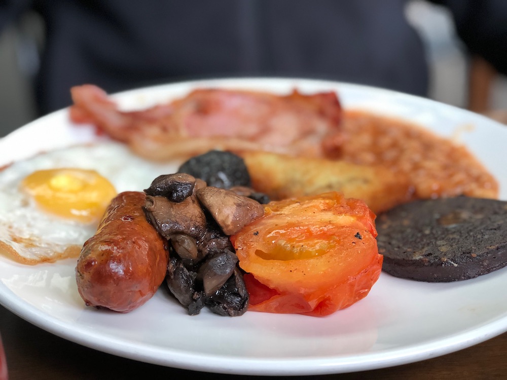 Photo of a traditional English breakfast recipe made with eggs, tomato, sausage, bacon, mushrooms, black pudding and beans.